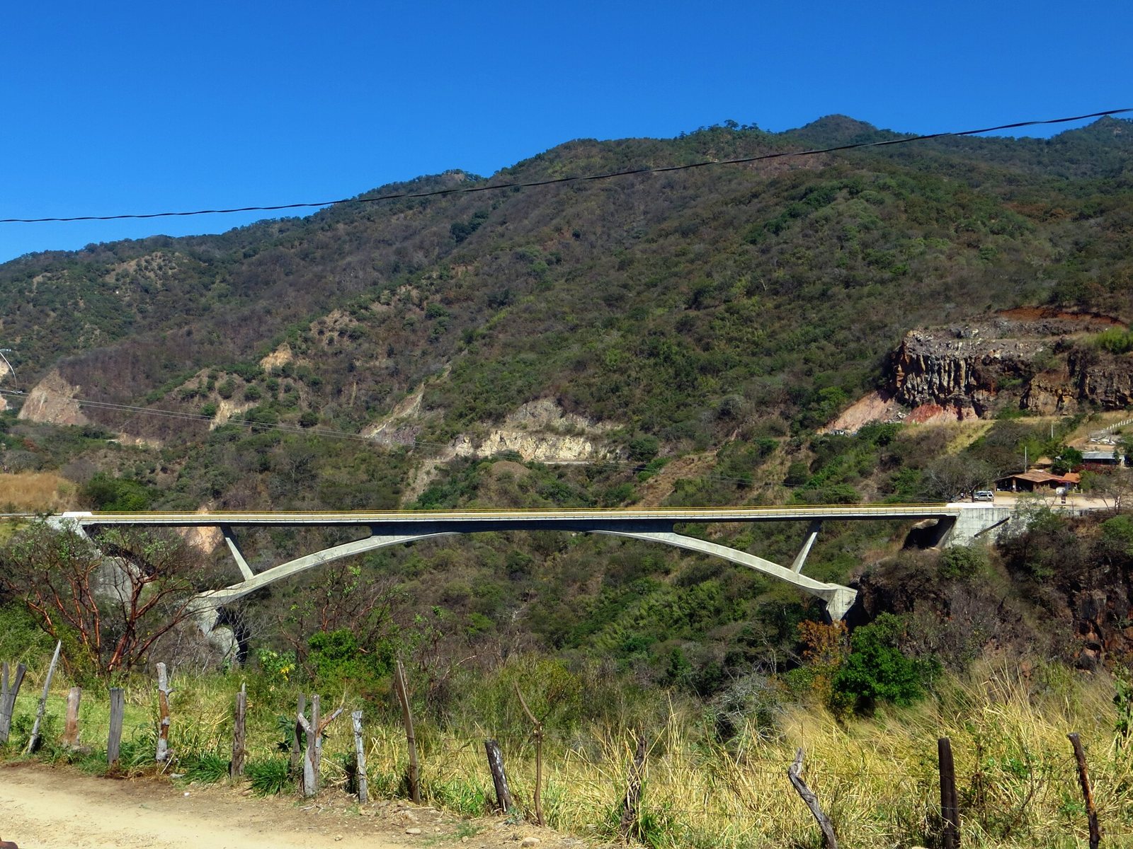 Puente de arco de concreto que cruza una barranca entre cerros con vegetación de la sierra