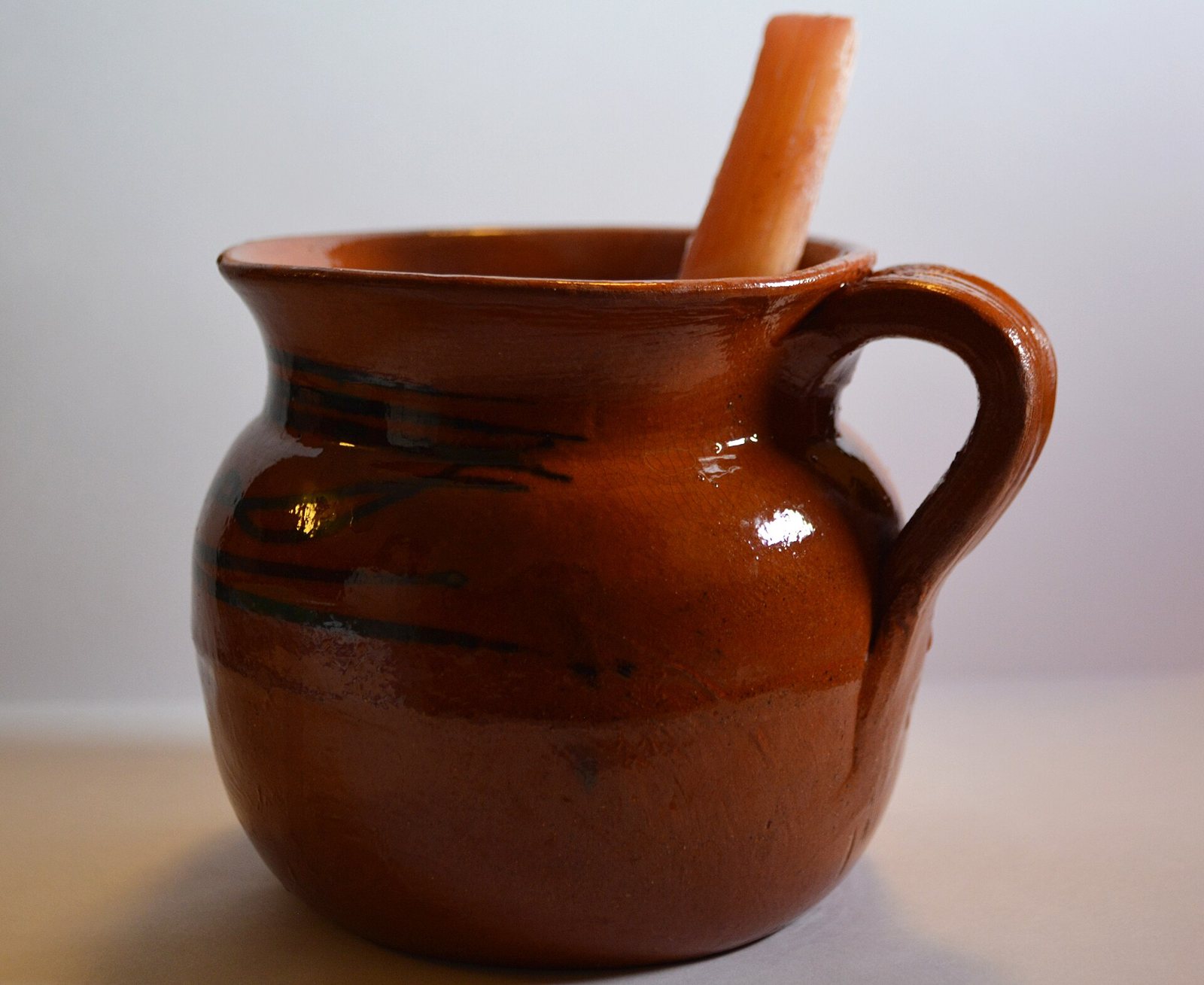 Jarrito de barro vidriado con ponche de frutas y un trozo de caña de azúcar
