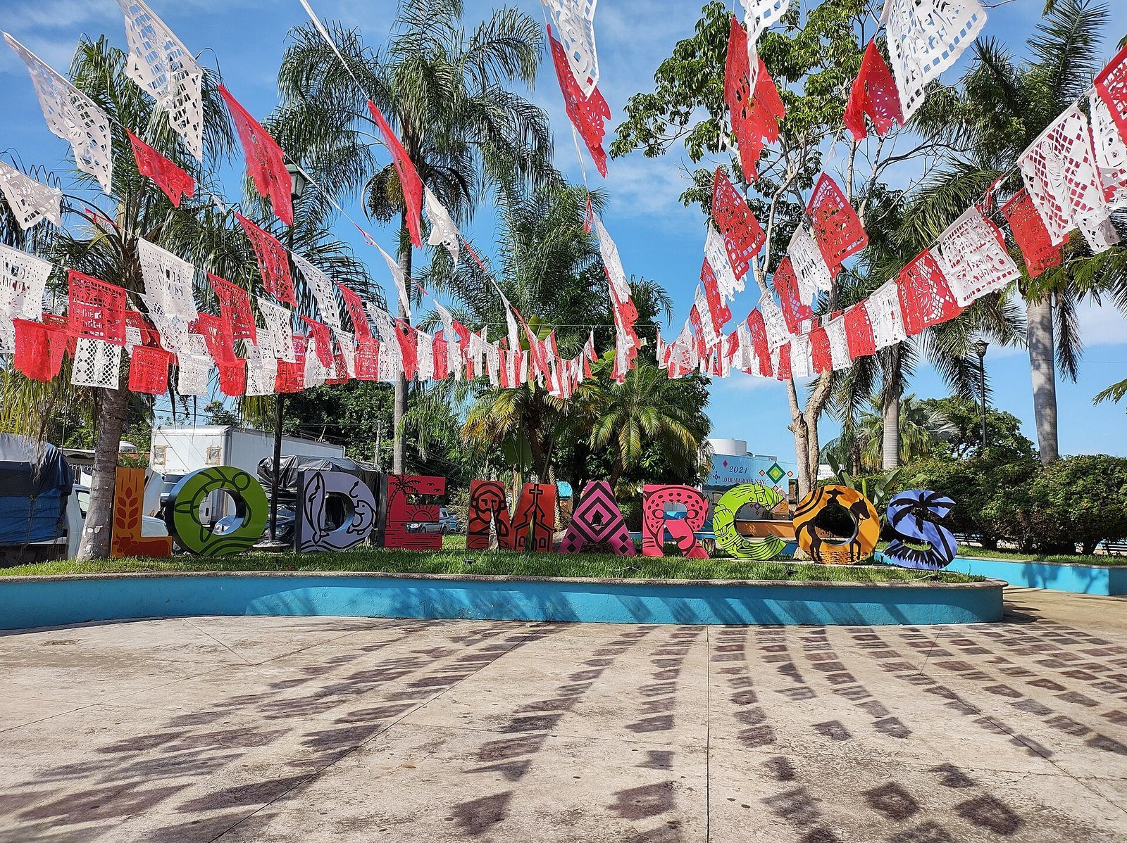 Letras de colores con el nombre de Lo de Marcos en la plaza, bajo papel picado