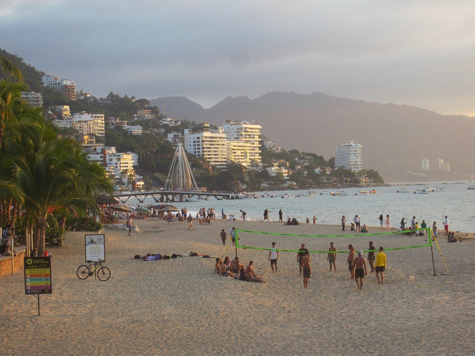 Playa Los Muertos al atardecer con gente jugando voleibol y el muelle al fondo