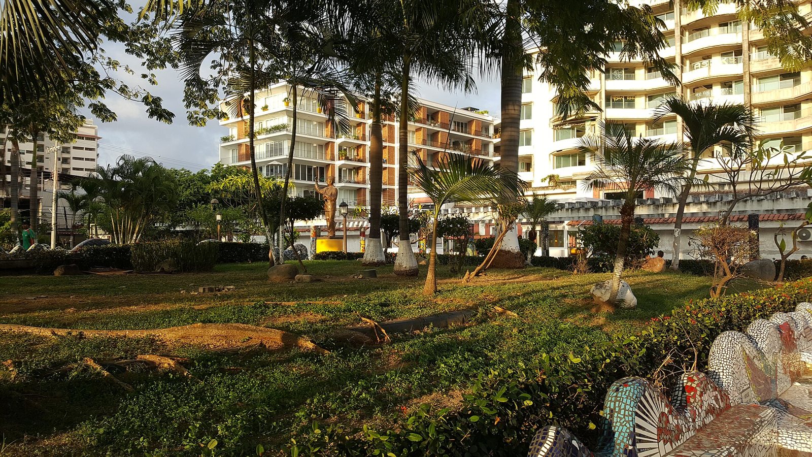 Parque Lázaro Cárdenas con palmeras, la estatua dorada del expresidente y bancas de mosaico en primer plano