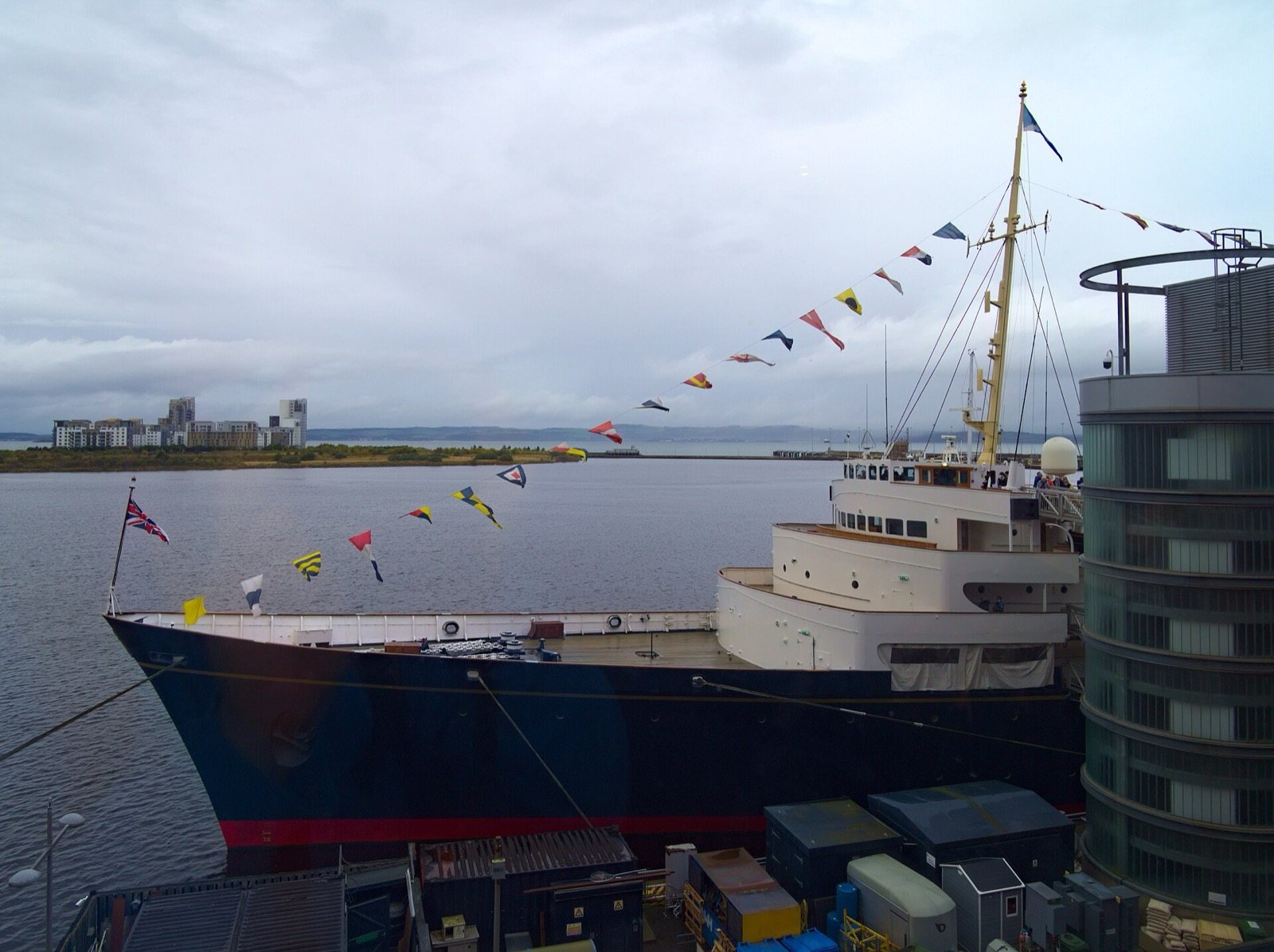Proa del yate real Britannia, de casco azul oscuro, atracado en el puerto de Leith con banderines de señales