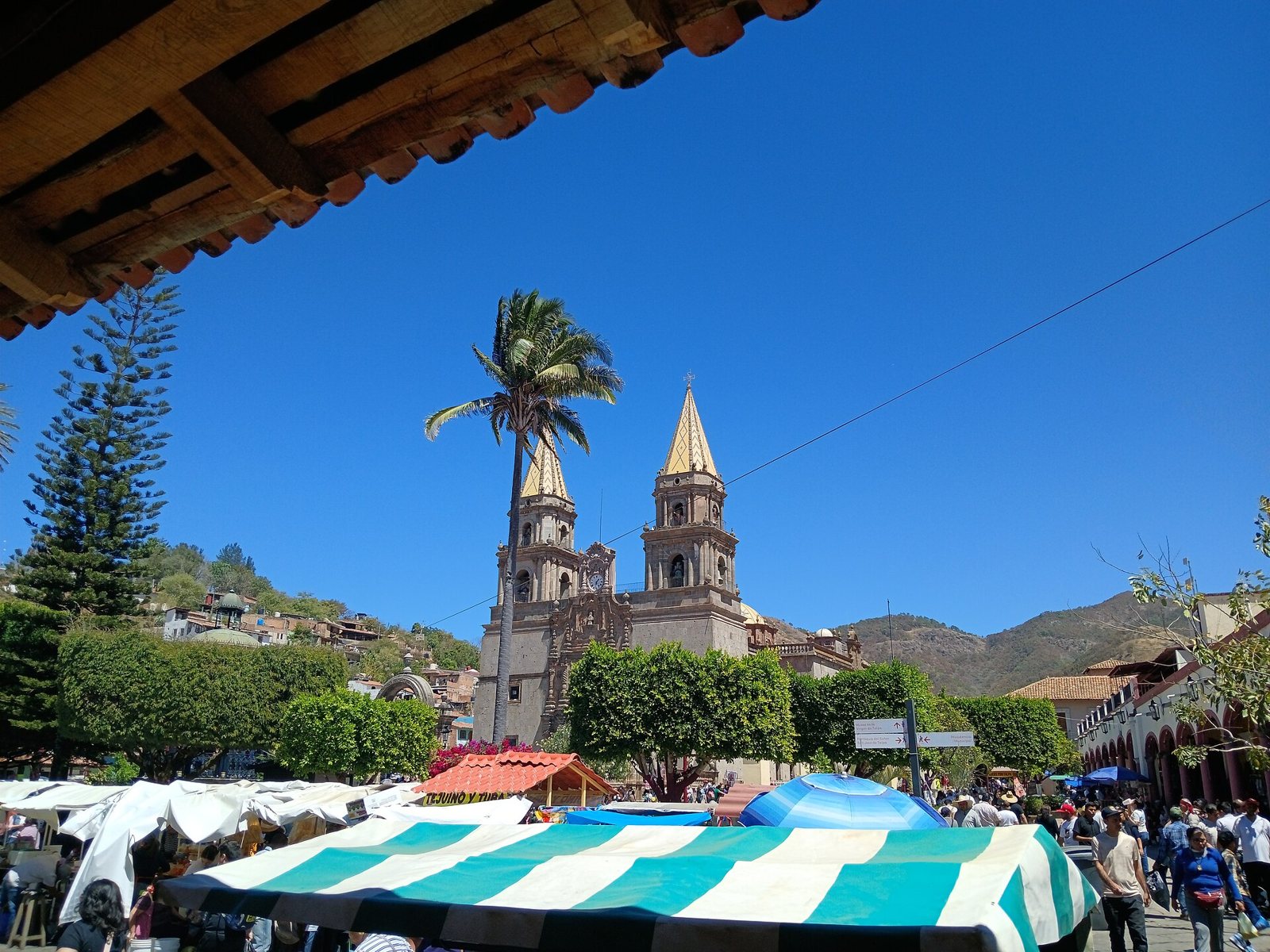 Basílica de Nuestra Señora del Rosario de Talpa con sus dos torres de cantera, una palmera y puestos del mercado en la plaza