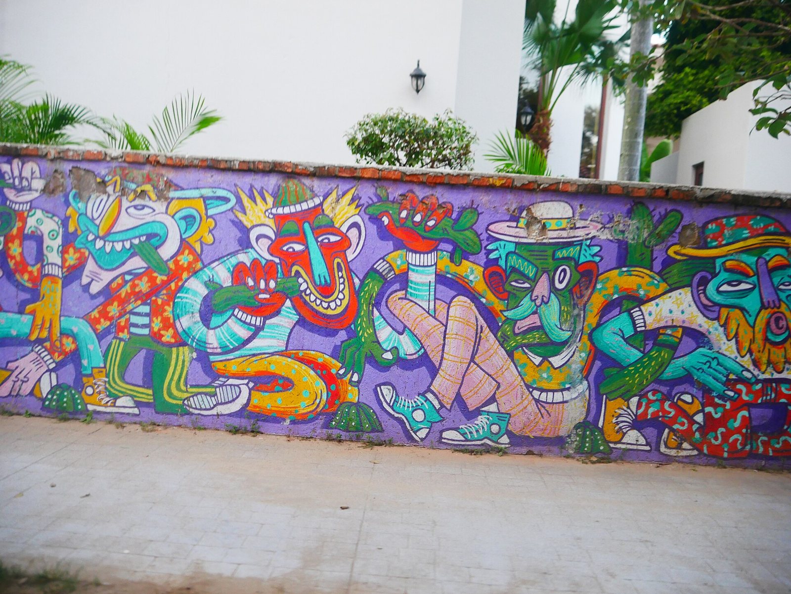 Mural de colores sobre una barda morada con personajes caricaturescos de sombrero, cerca de la entrada a la playa de San Pancho