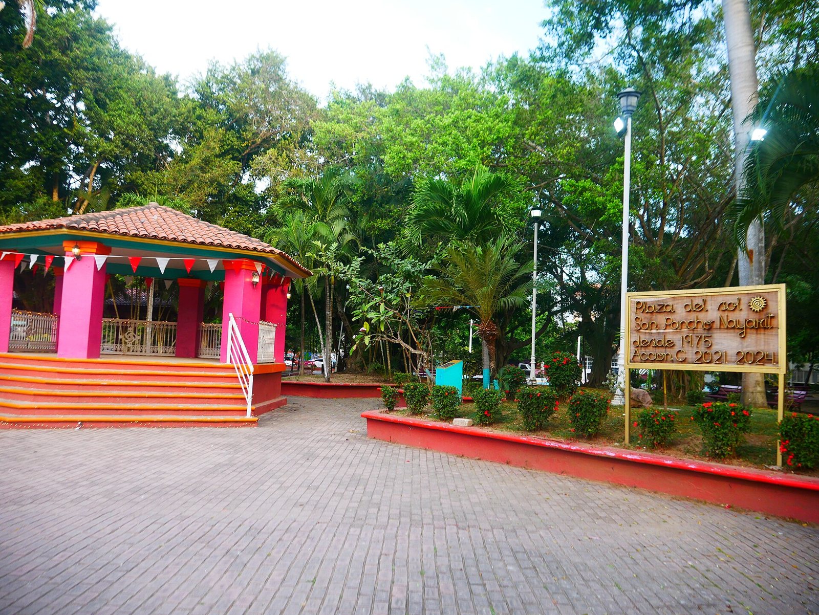 Kiosco rosa con techo de teja y letrero de madera de la Plaza del Sol de San Pancho, rodeado de árboles