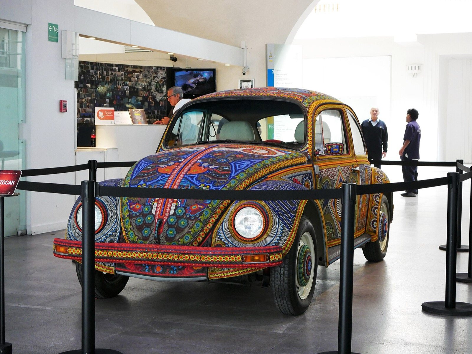 Vocho cubierto de chaquira con diseños de estilo huichol, exhibido detrás de un cordón en el vestíbulo de un museo