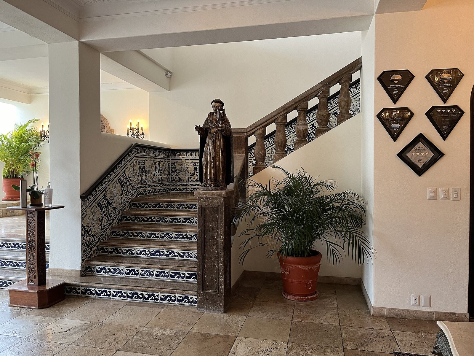 Escalera con azulejos azul y blanco, barandal de cantera y una escultura religiosa de madera en el vestíbulo de Casa Kimberly