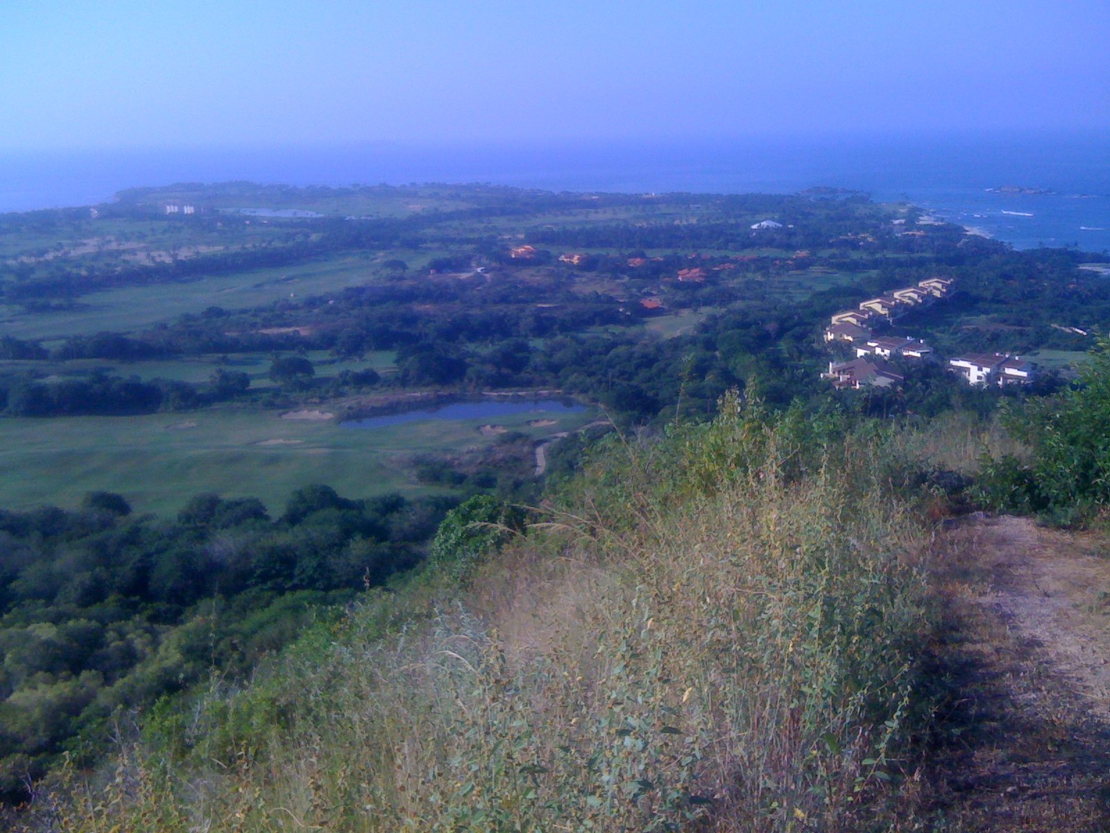 Vista desde un cerro de los campos de golf de Punta Mita, con un lago, villas entre la vegetación y el mar al fondo