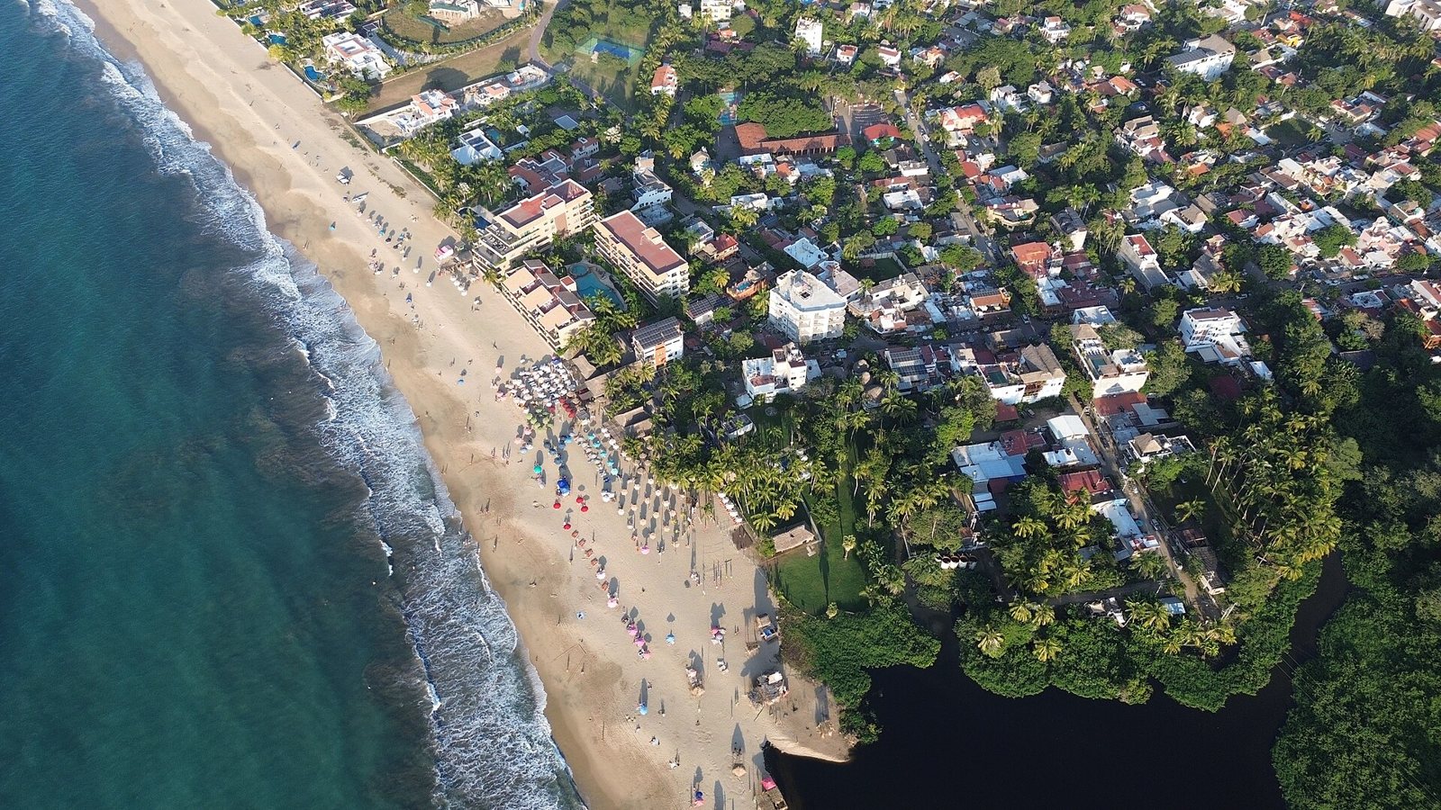 Vista aérea de la playa de San Francisco (San Pancho), Nayarit, con sombrillas de colores, palmeras, el pueblo y un estero junto al mar