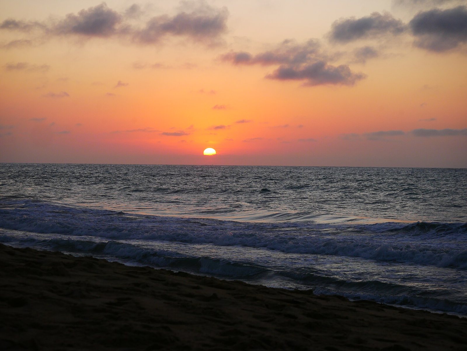 Sol ocultándose en el horizonte del Pacífico con cielo naranja y olas rompiendo en la arena de San Pancho