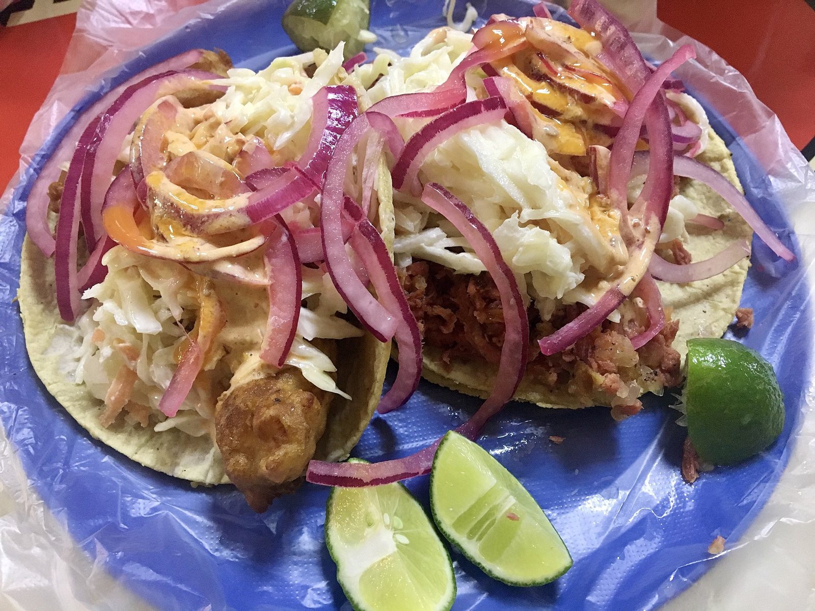 Dos tacos de pescado capeado con col, cebolla morada y aderezo cremoso, servidos con limones