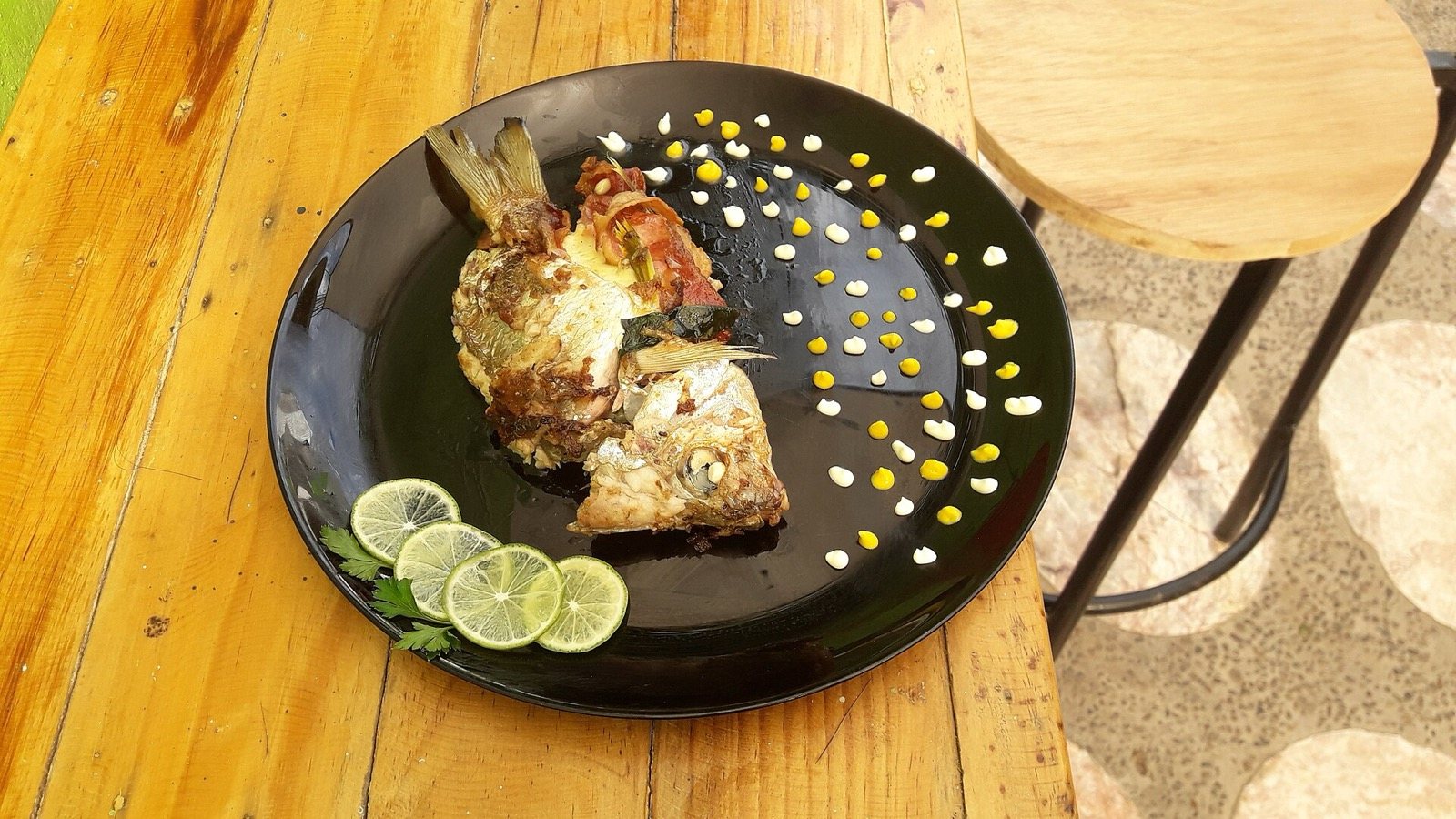 Pescado zarandeado servido en plato negro con rodajas de limón sobre una mesa de madera
