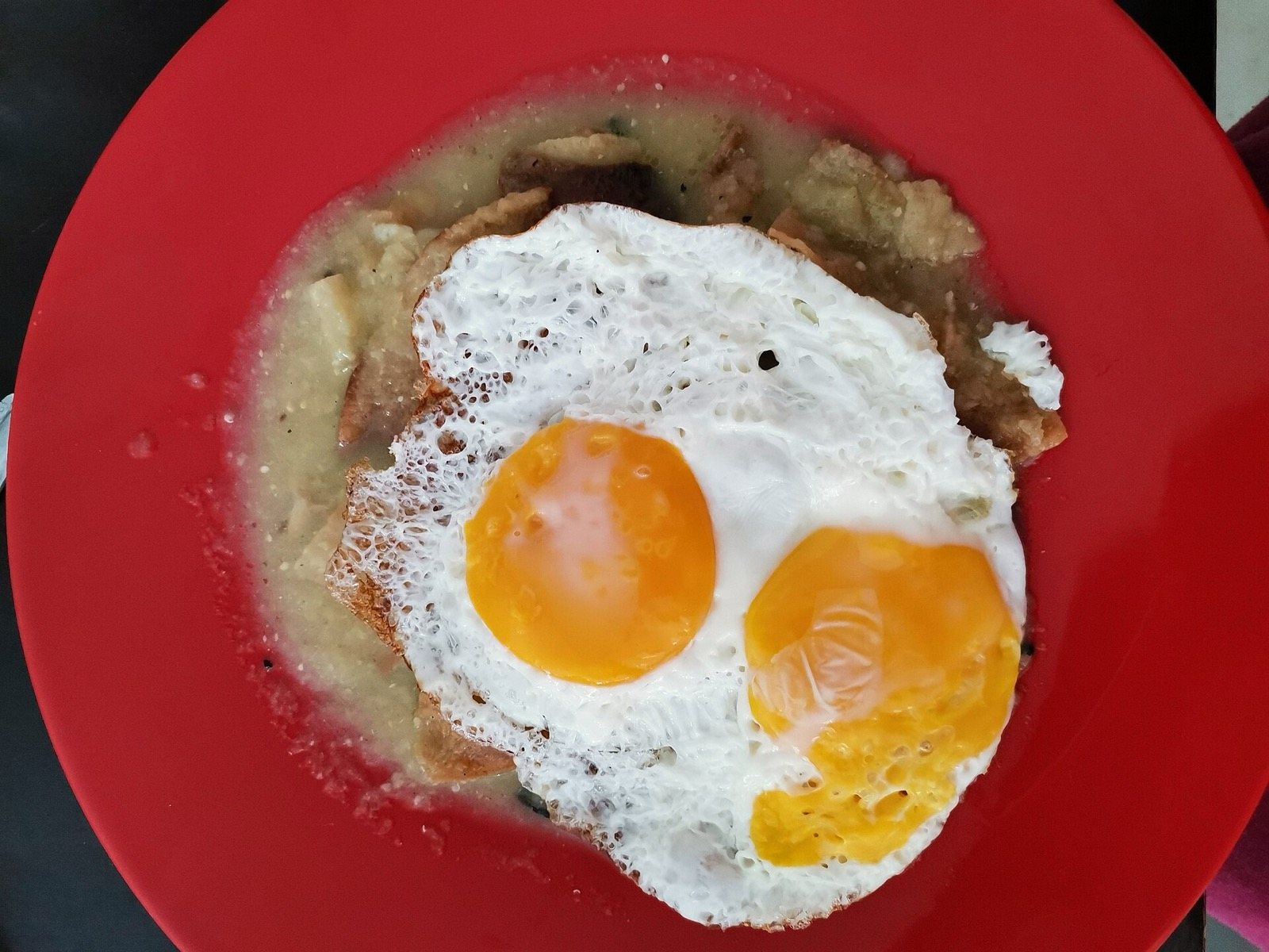 Plato rojo con chilaquiles en salsa verde cubiertos con dos huevos estrellados