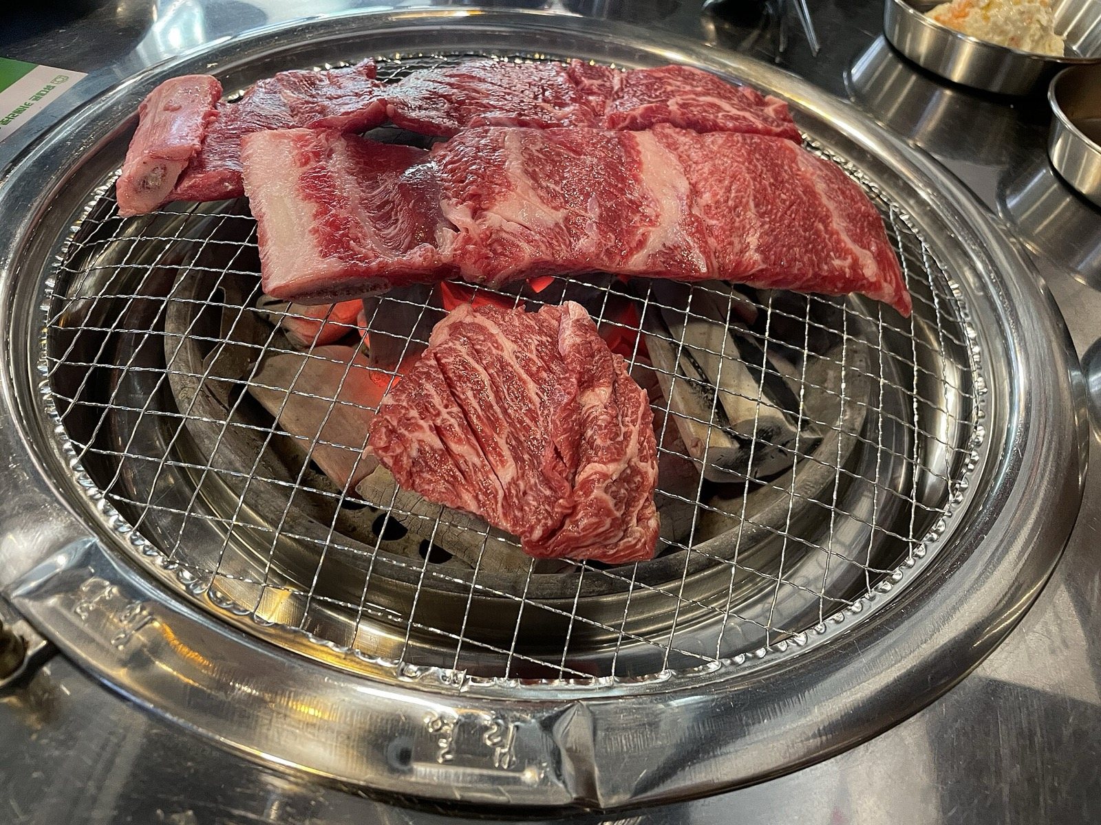 Cortes de res marmoleados asándose sobre una parrilla de carbón en la mesa, al estilo coreano