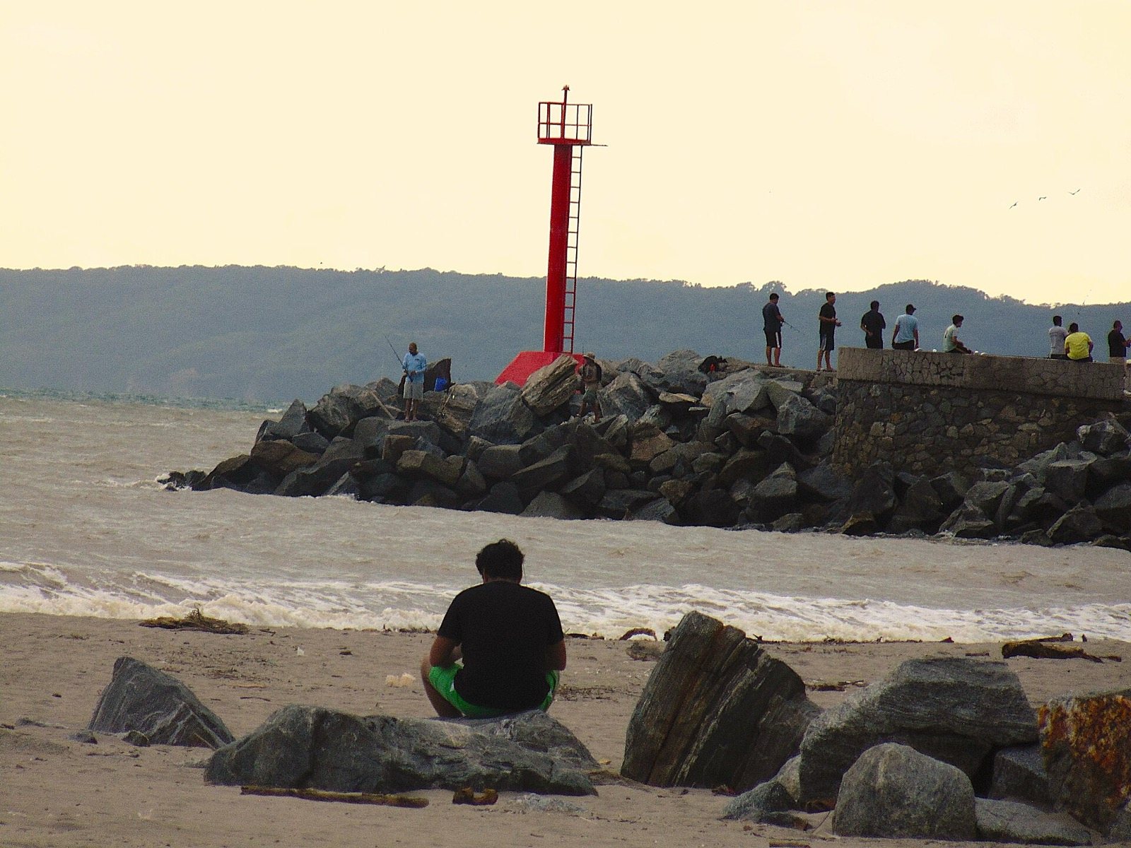 Faro rojo sobre la escollera de la marina de Nuevo Vallarta, con personas pescando y la sierra al fondo