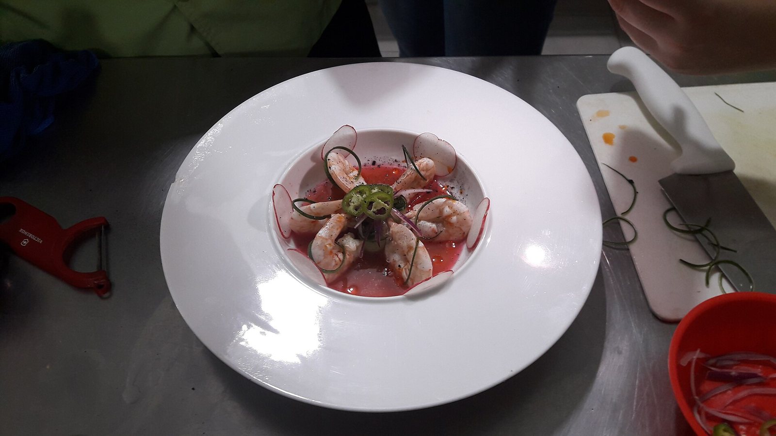 Plato hondo blanco con camarones en caldo rojo de chile y limón, rodajas de rábano y chile en rueda