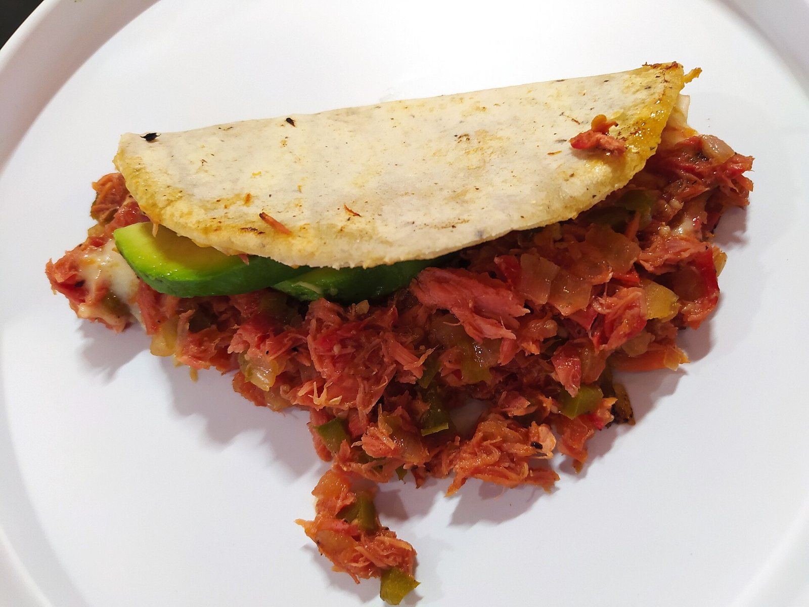 Quesadilla de tortilla de maíz rellena de marlín guisado con jitomate y pimiento, con una rebanada de aguacate