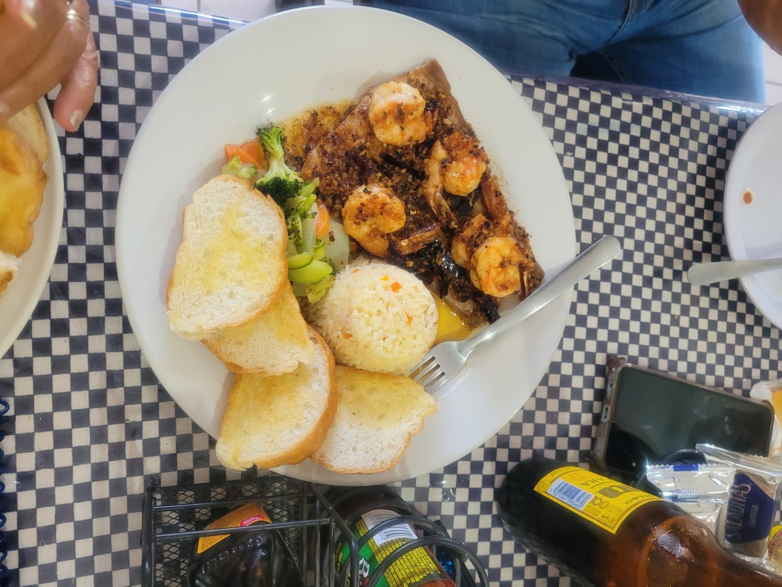 Plato de camarones al ajillo con arroz, verduras y pan tostado sobre un mantel de cuadros