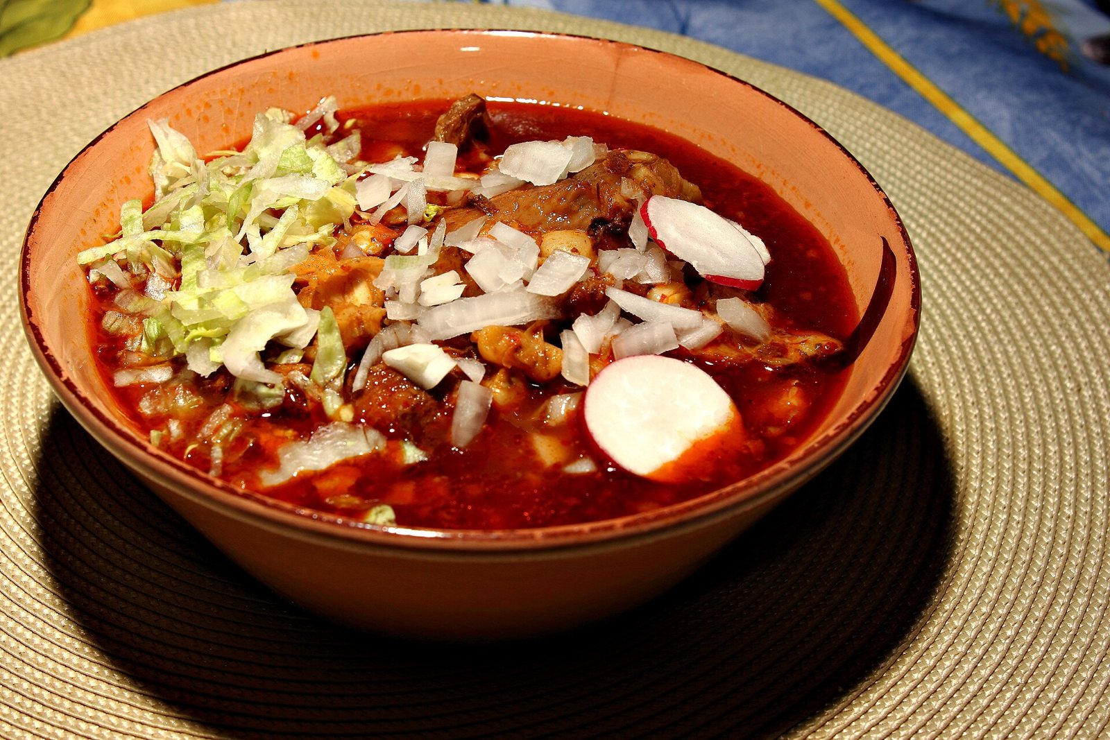 Tazón de pozole rojo con carne de cerdo y maíz, lechuga, cebolla picada y rodajas de rábano