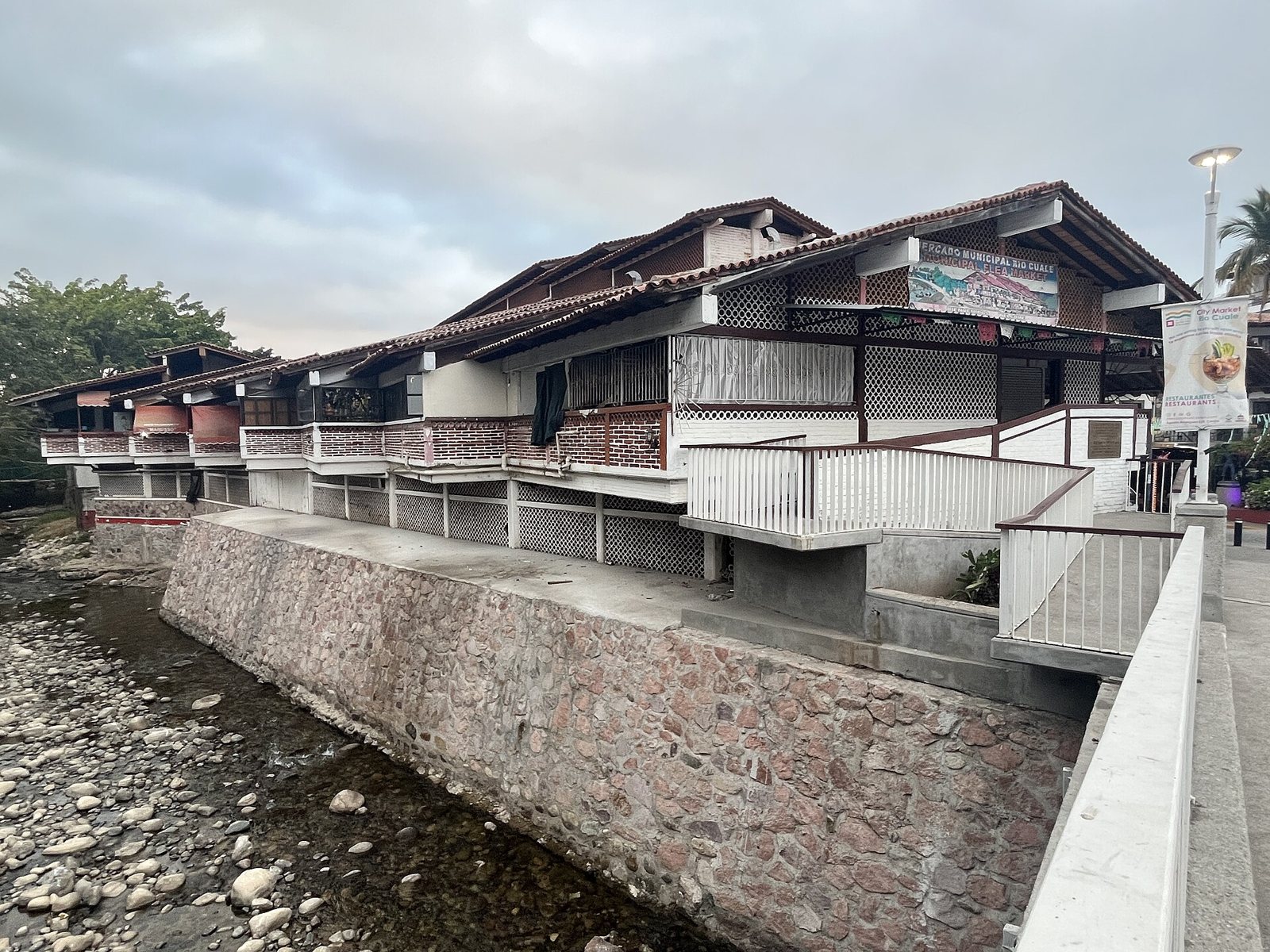 Edificio del Mercado Municipal Río Cuale con balcones y techos de teja, construido sobre un muro de piedra a la orilla del río Cuale