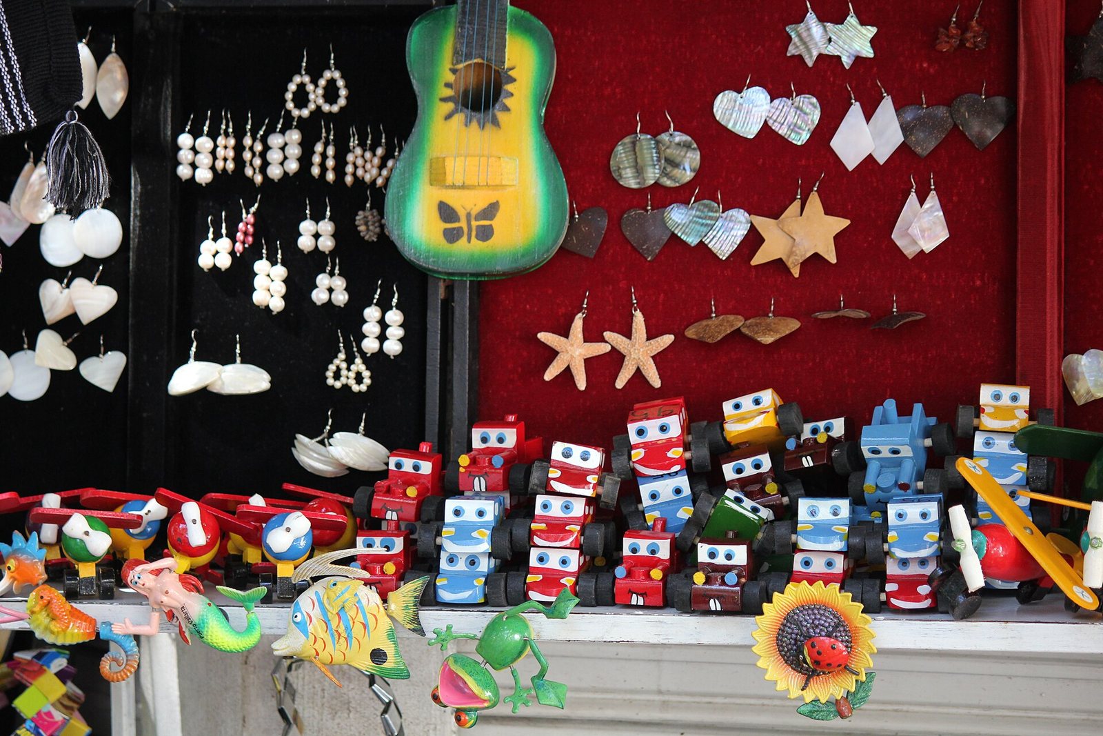 Puesto de artesanías con aretes de concha y nácar, una guitarra de juguete pintada, carritos de madera de colores e imanes de animales marinos