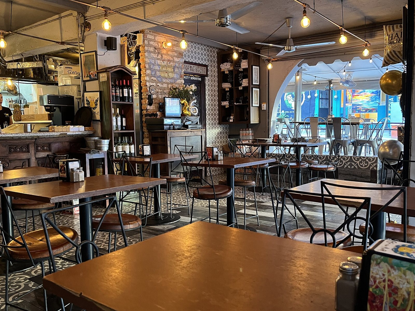 Interior de Café San Ángel con mesas de madera, sillas de herrería, piso de mosaico, focos colgantes y una barra con cafetera