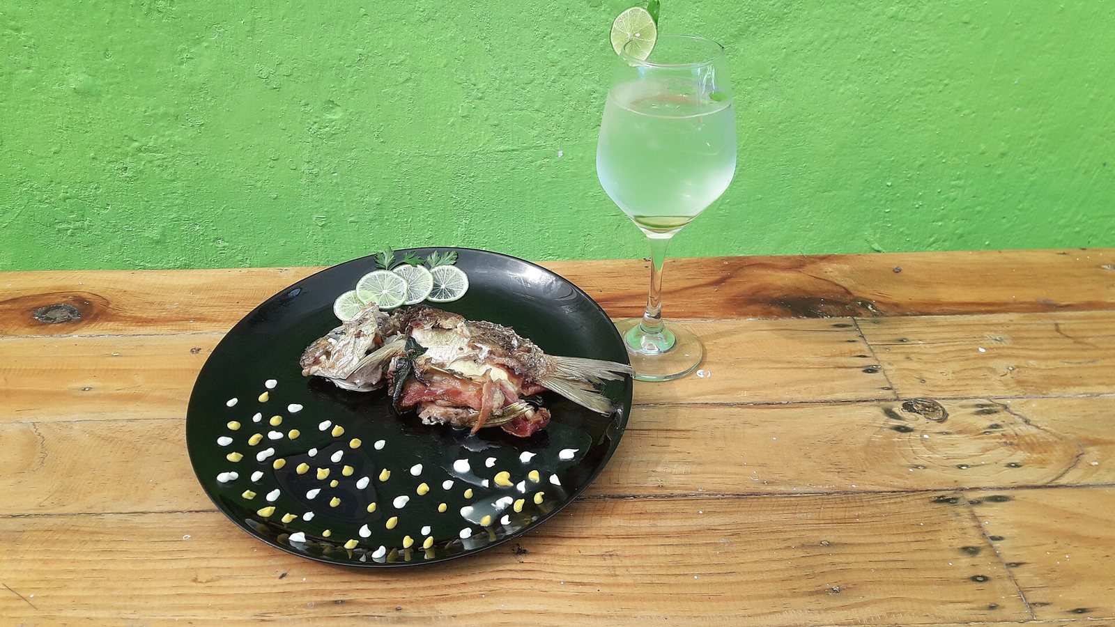 Pescado entero asado servido en un plato negro con rodajas de limón, junto a una copa de agua
